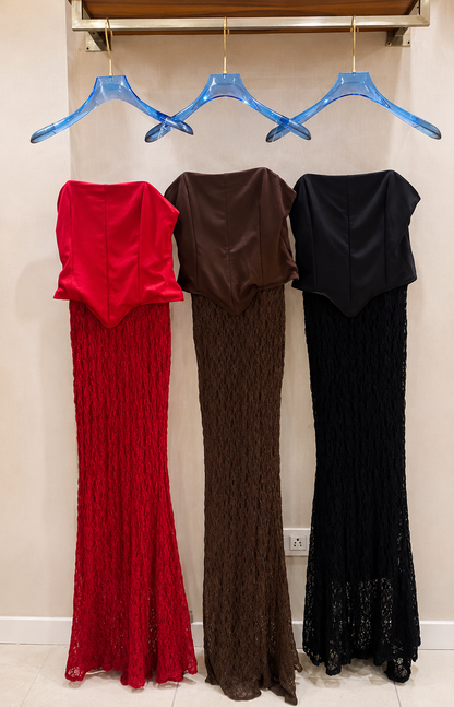 Three long dresses in red, brown, and black hanging on blue hangers against a beige wall.